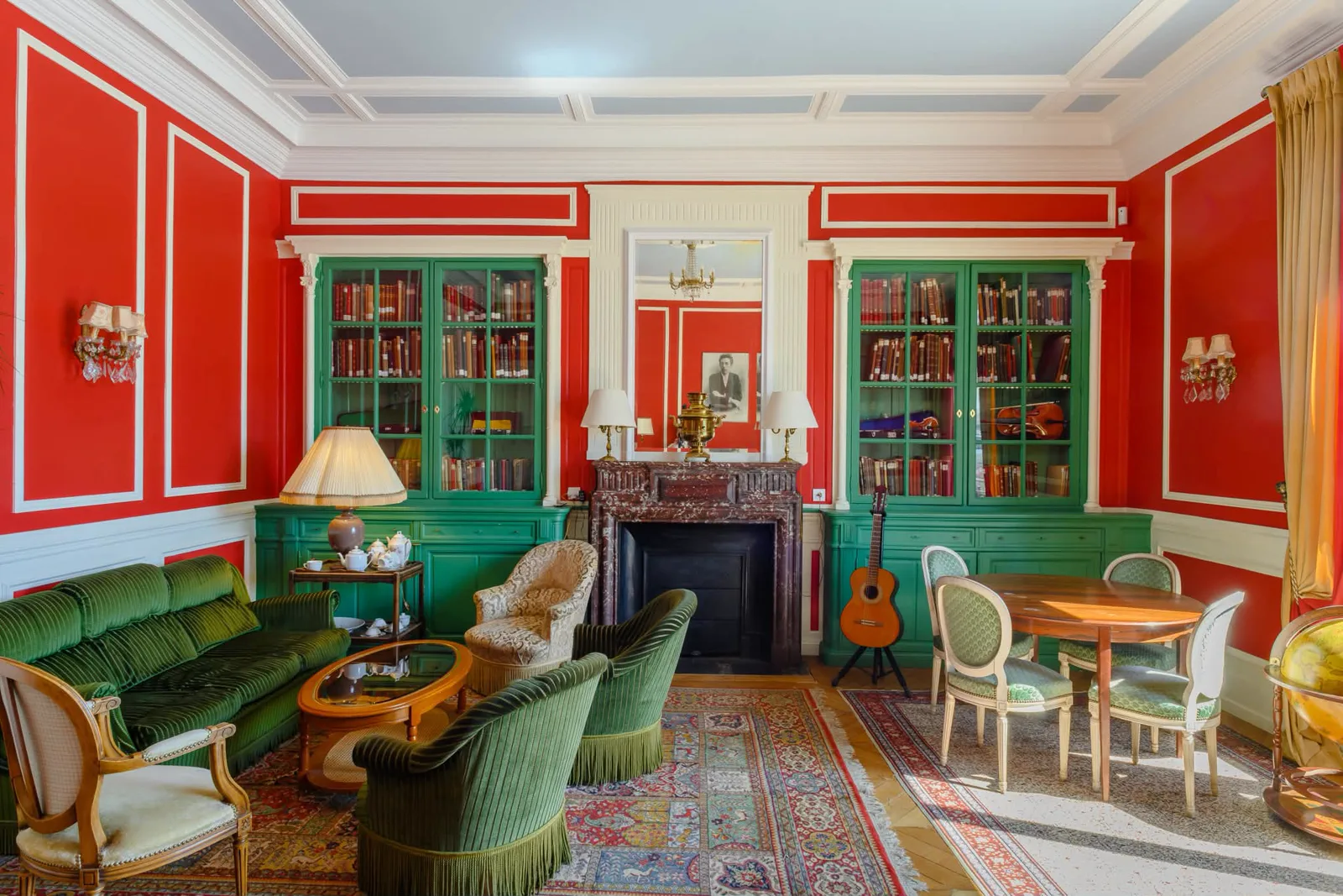 Salon de bibliothèque aux boiseries vertes et murs vermillon, mobilier d'époque